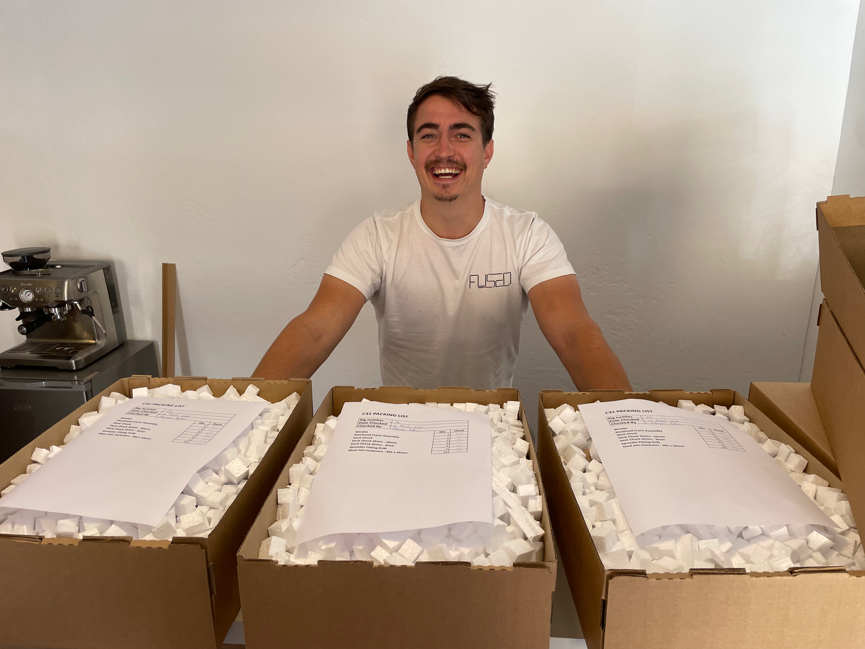Adriaan smiling behind three open boxes of packed components ready for dispatch