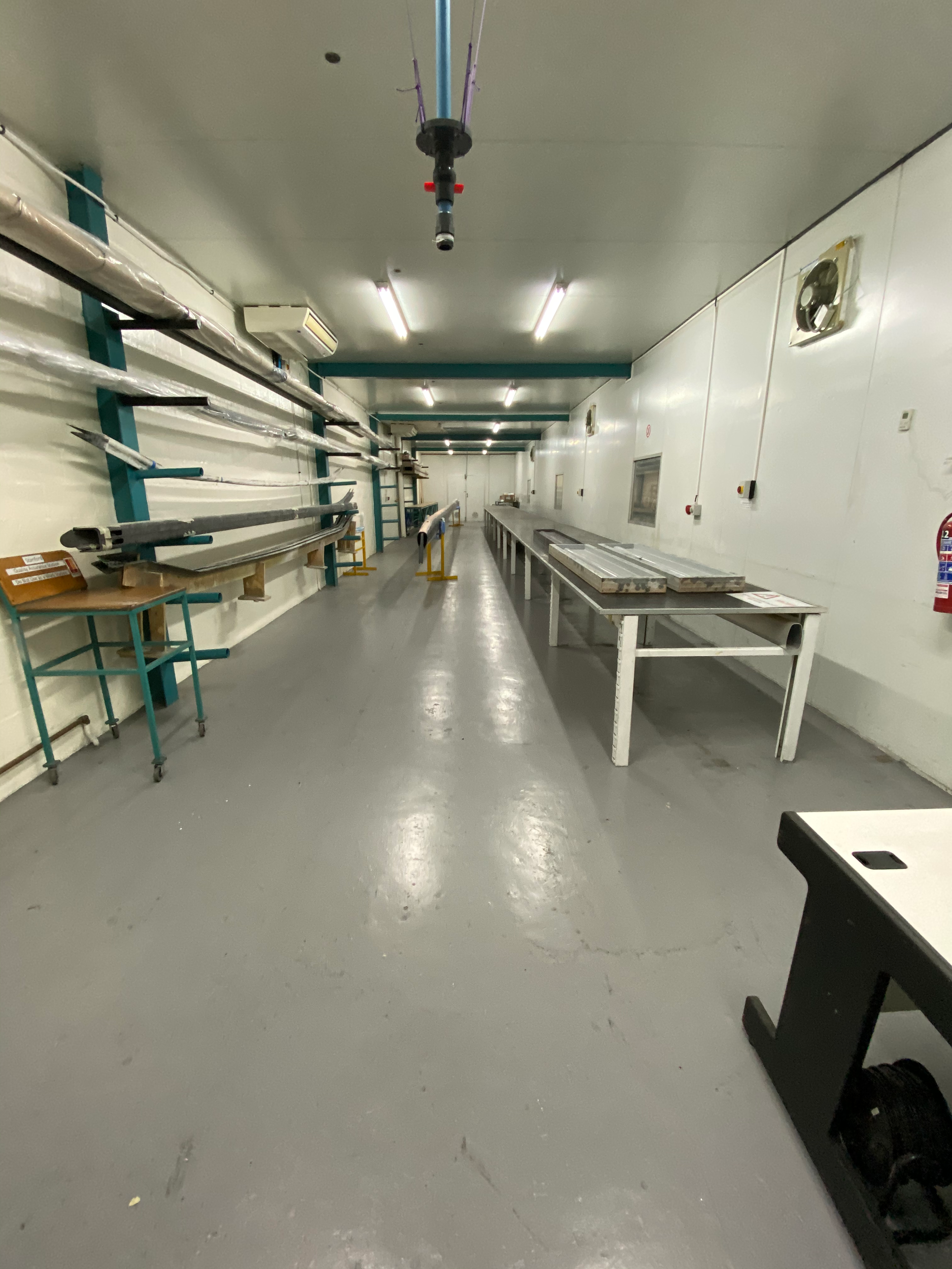 A long empty industrial workshop with a single workbench and bare racking