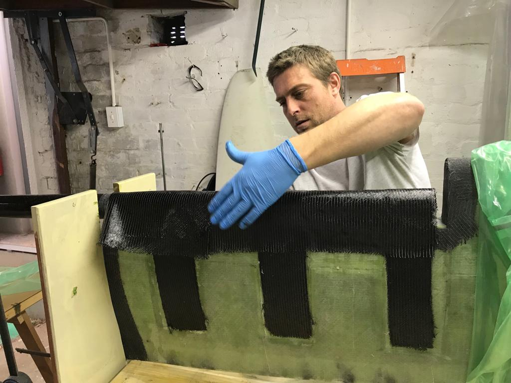 Wilhelm Botha in blue gloves pressing carbon fibre strips onto a laminate in a small workshop