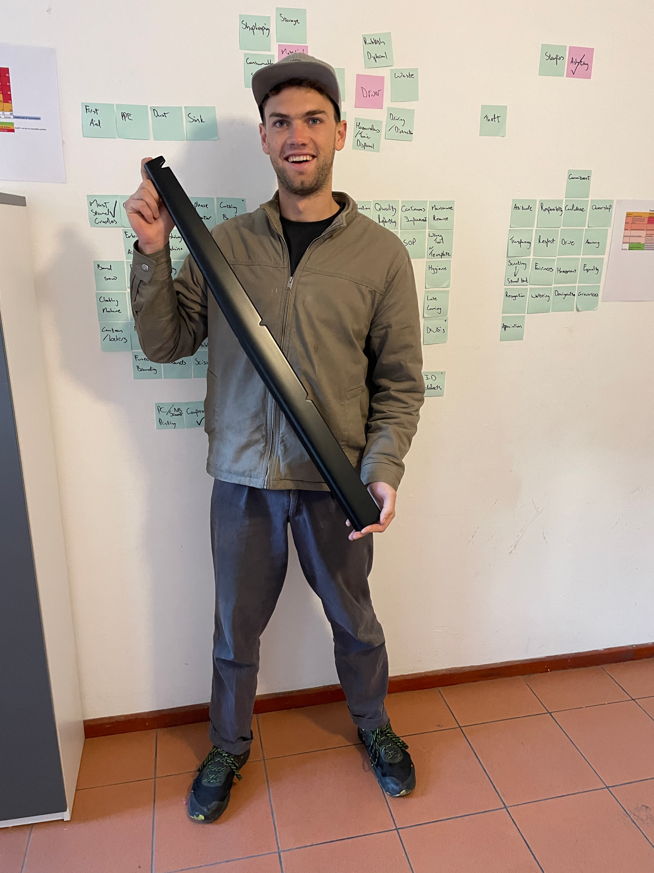 Thomas holding a slim black carbon fibre section in front of a wall covered in sticky notes