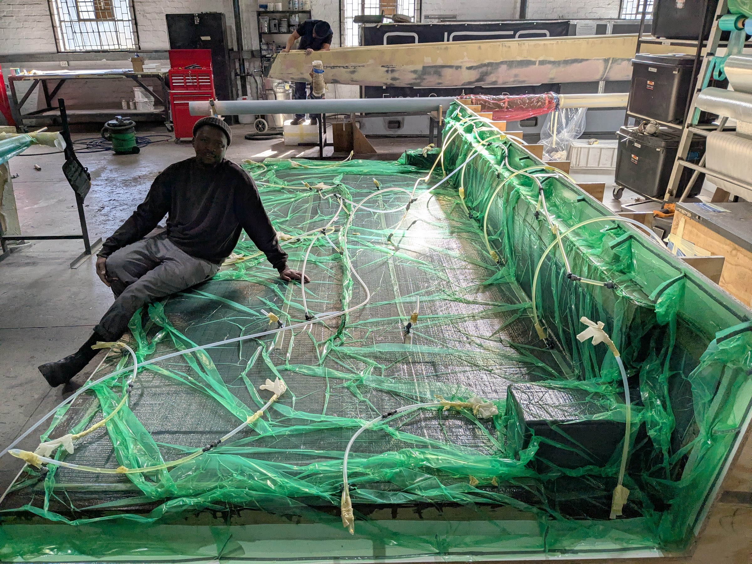 Large mould sealed under green vacuum film with lines in place, technician beside it