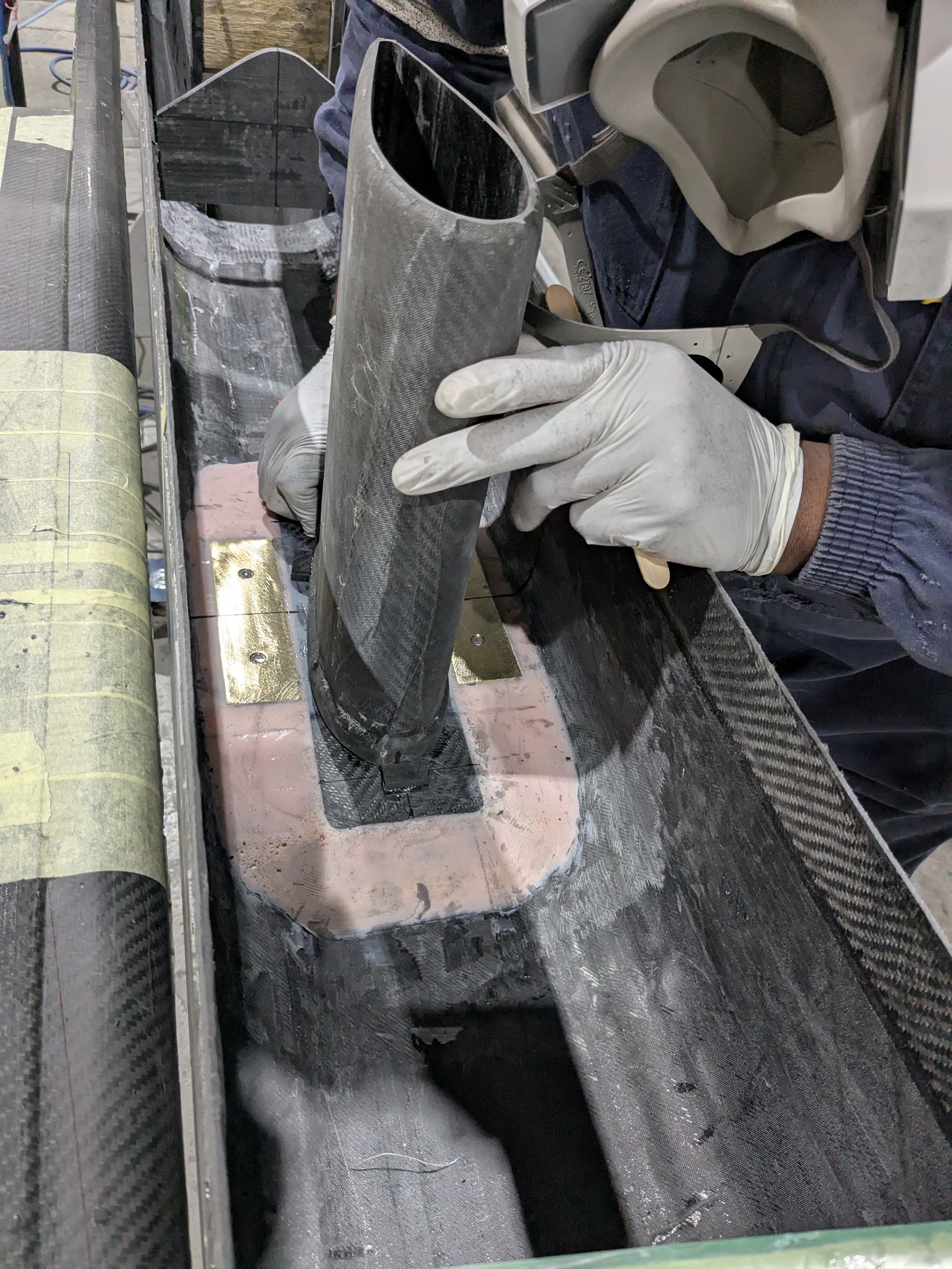 Gloved hands fitting a carbon tube into a recess in a beam inside the mould