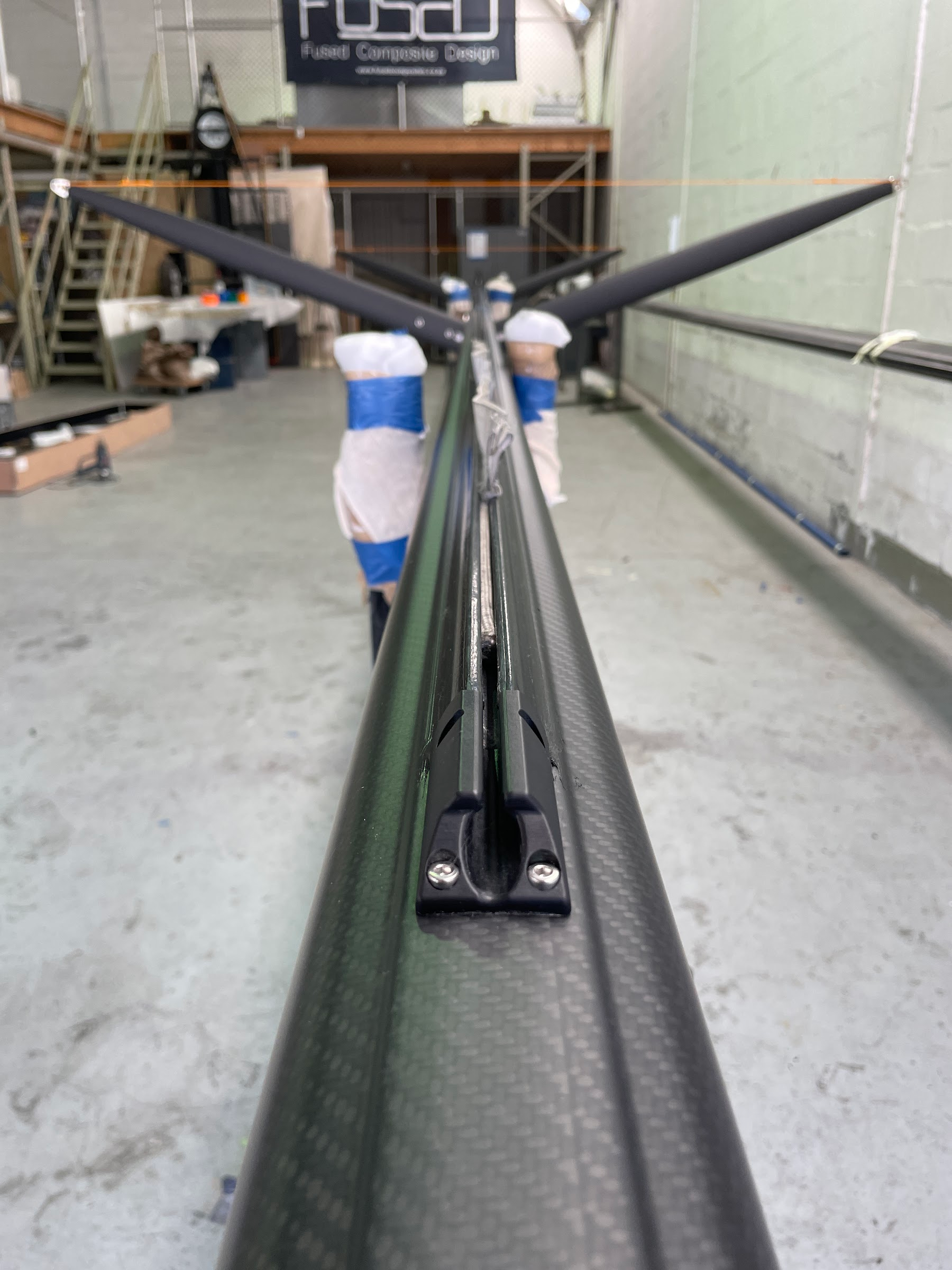 Carbon fibre mast with spreaders lying on a factory floor, viewed along its length